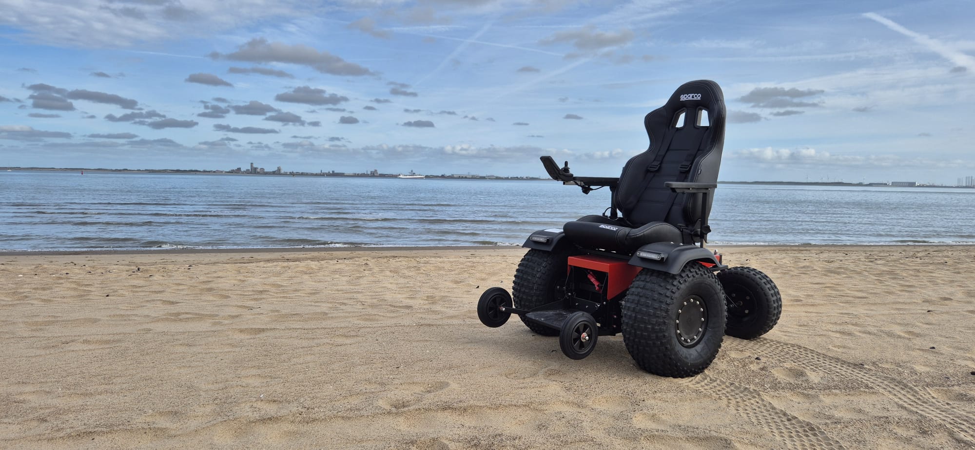 Elektrische strandrolstoel met grove terreinbanden op het strand in de gemeente Sluis bij laag water